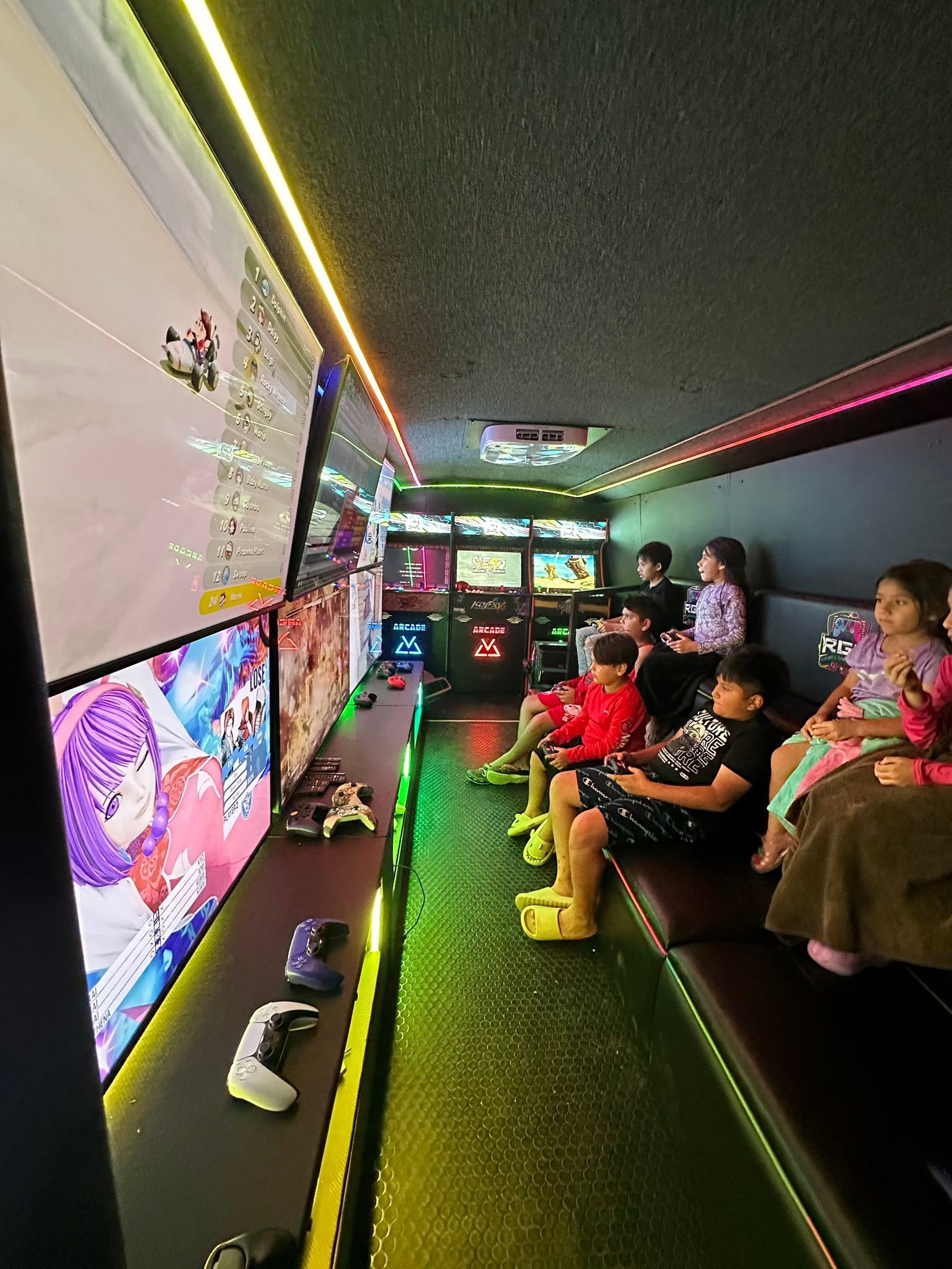A group of kids seated along the bench playing at the gaming stations inside the RGV Games on Wheelz bus