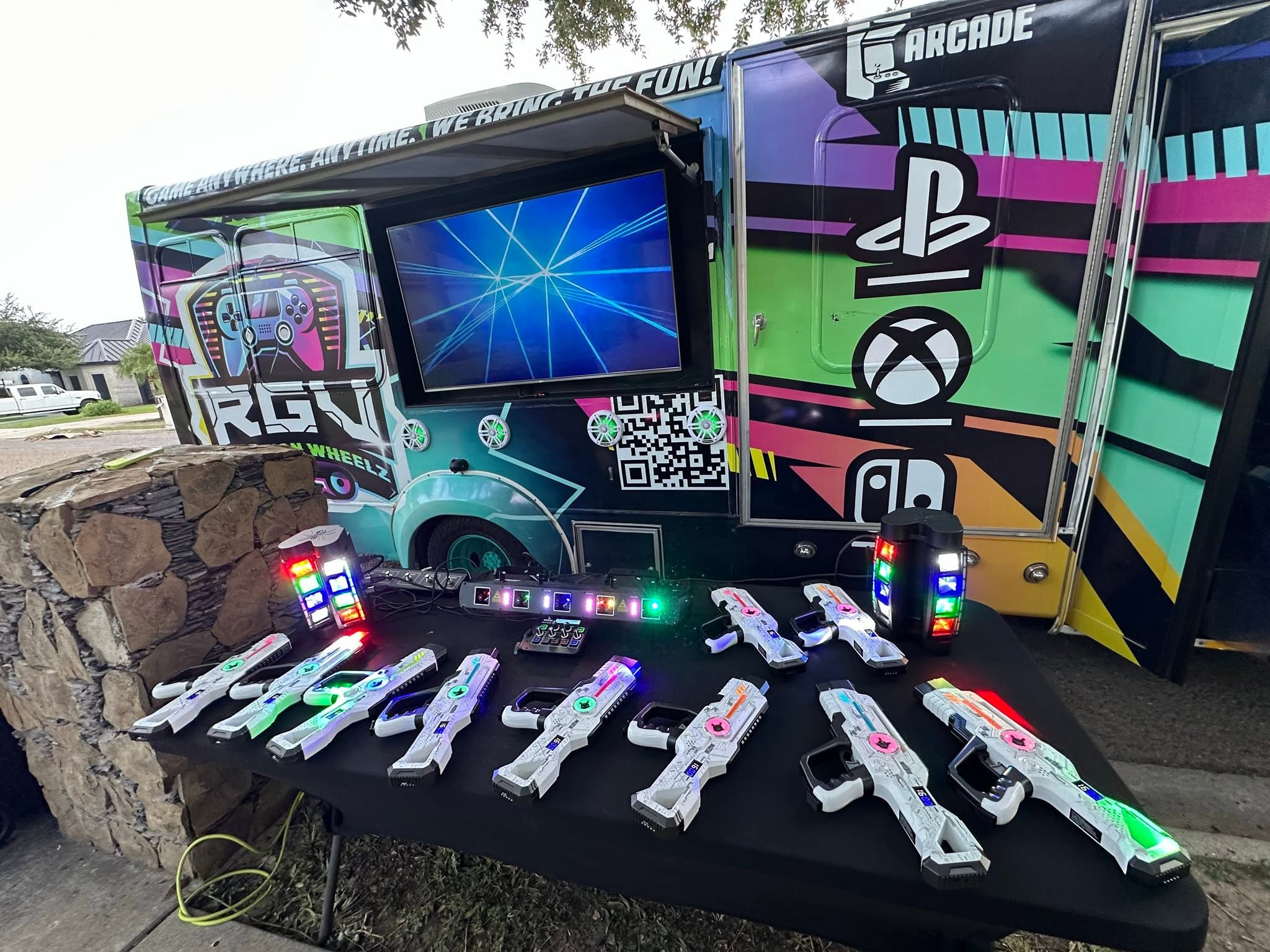 Laser tag blasters laid out on a table beside the RGV Games on Wheelz mobile gaming bus before an event
