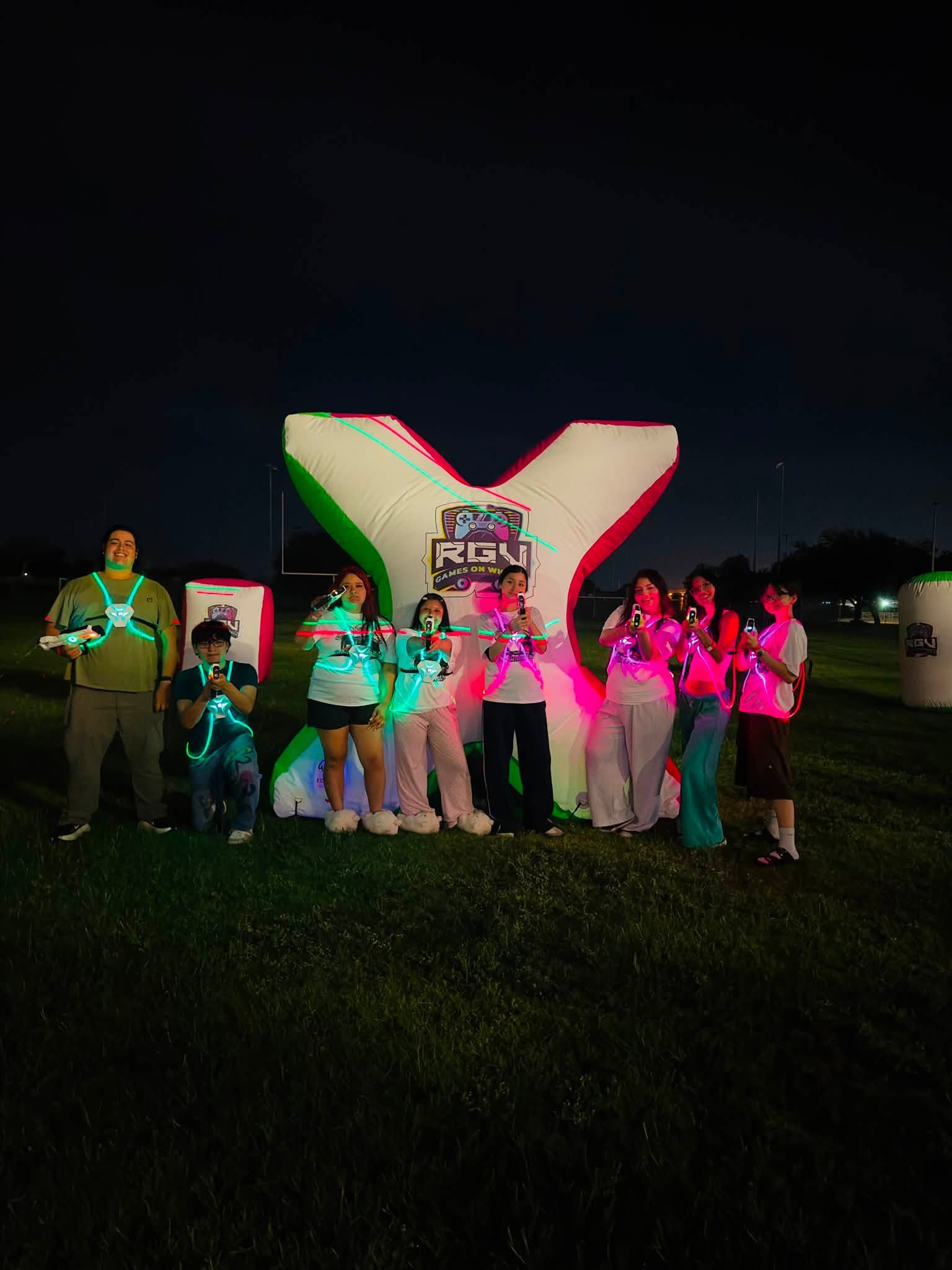 A group in light-up laser tag vests gathered around a glowing inflatable bunker at an RGV Games on Wheelz night game
