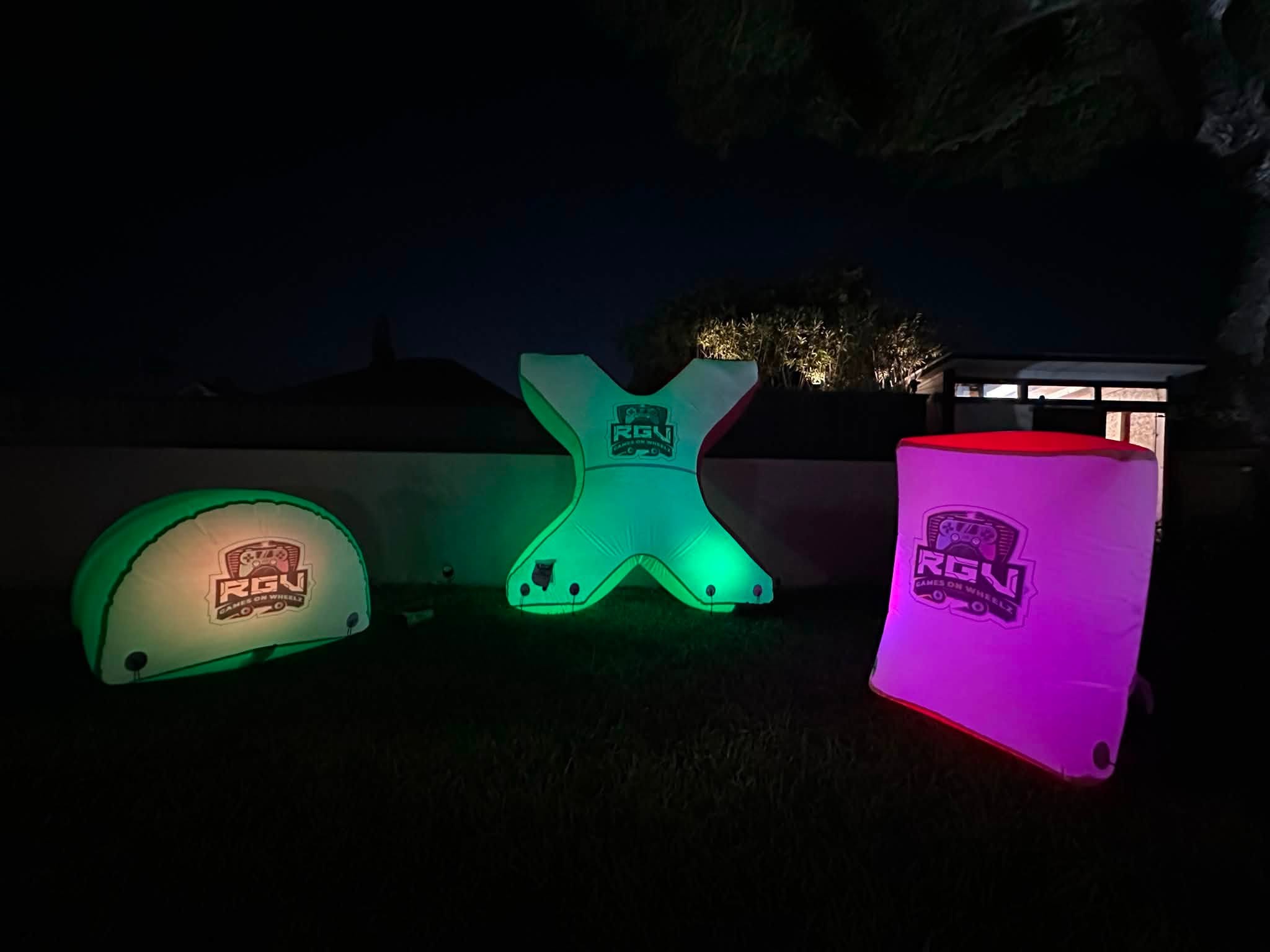 Glowing inflatable laser tag bunkers set up on a field at night for an RGV Games on Wheelz mobile laser tag game