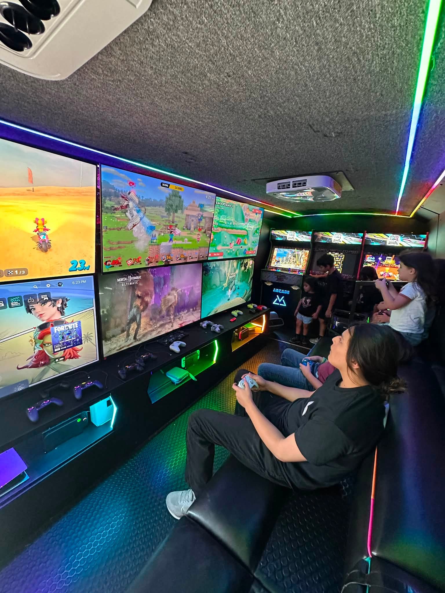 Players on the bench seating using controllers at the lit screen wall inside the RGV Games on Wheelz gaming bus