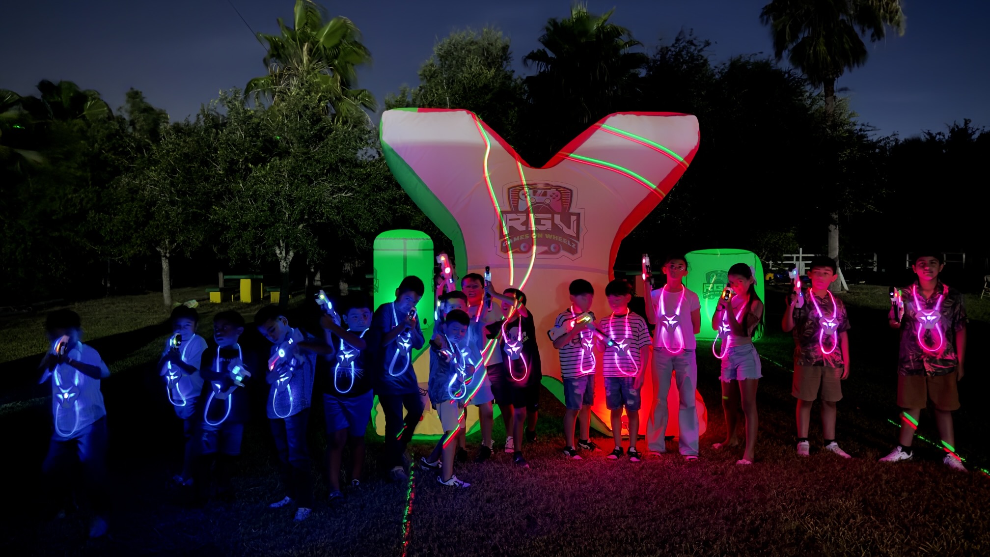 A large group in light-up laser tag vests gathered on a field at night for an RGV Games on Wheelz event