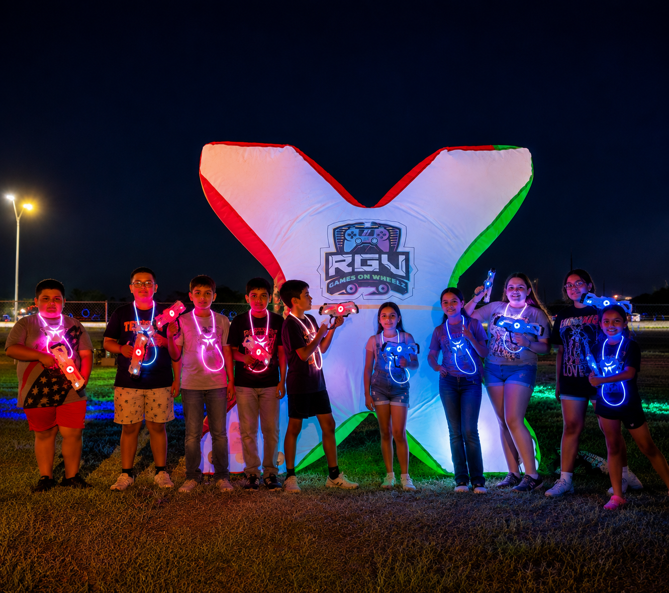 Players in glowing laser tag vests lined up beside an inflatable bunker at an RGV Games on Wheelz night game