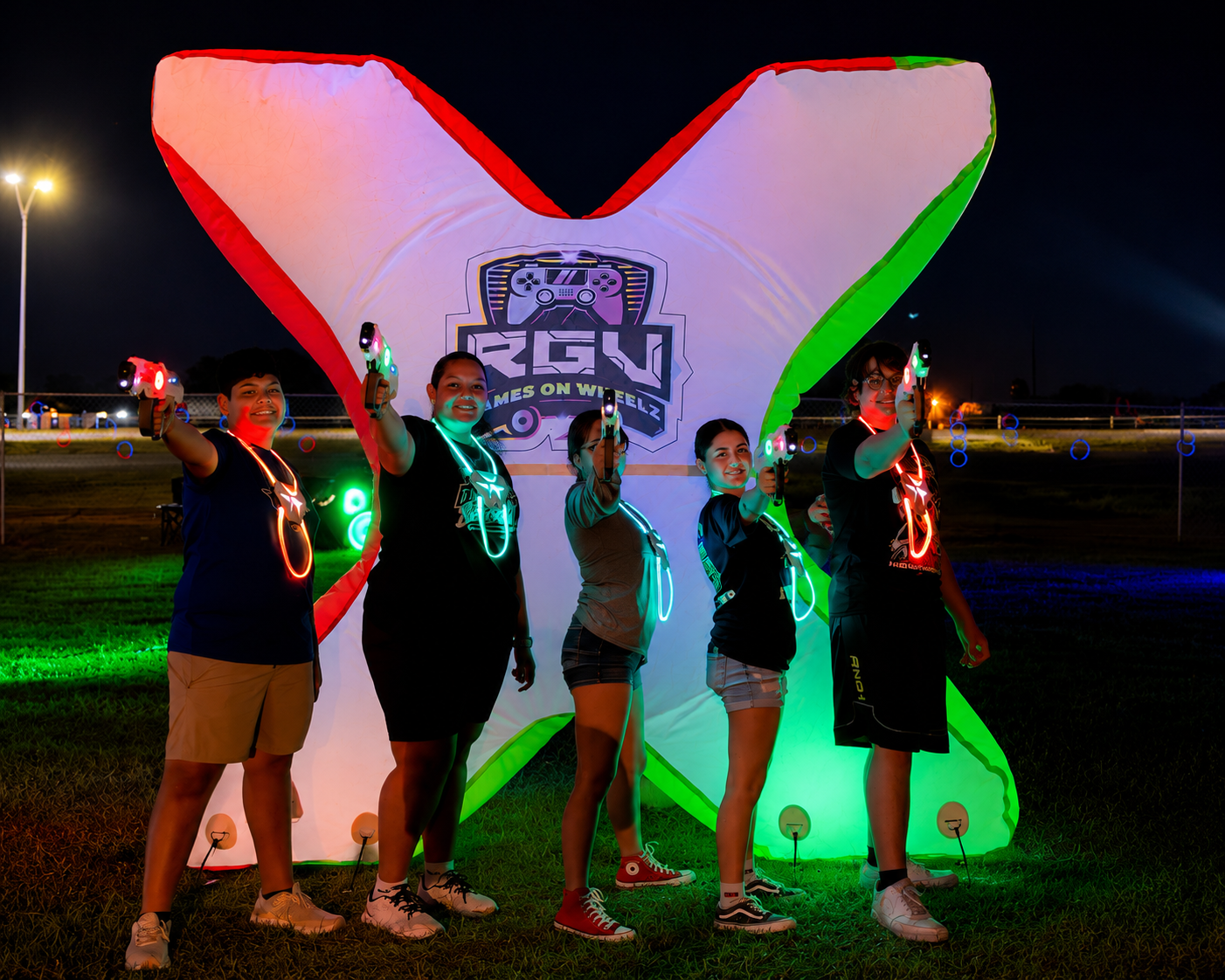 Players in light-up vests holding laser tag blasters beside a glowing inflatable bunker at an RGV Games on Wheelz night game